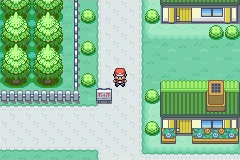 The player standing beside a sign near a house, trees and a paved path.